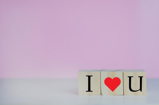 Wooden cubes with i love u symbol heart on the pink background and copy space.