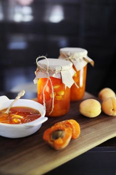 apricot jam with almonds in a white bowl with a miniature spoon against the background of two jars of jam - conservation. vertical photo, black background
