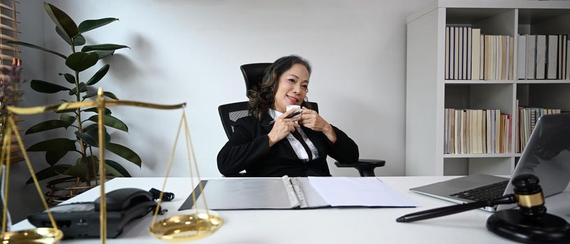 Mature female lawyer drinking coffee, resting at her personal office.