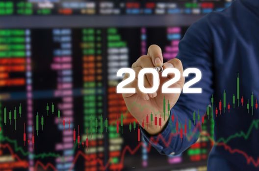 hand hold pen touching screen digital virtual futuristic interface 2022 New year candlestick graph chart auto trade, business finance investment stock exchange market concept background.