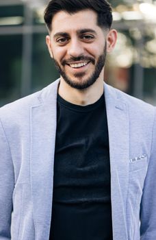 Face of handsome positive bearded businessman corporate leader boss executive successful employer smiling at camera with building at the background. Businessperson portrait. Entrepreneur. Expressions.