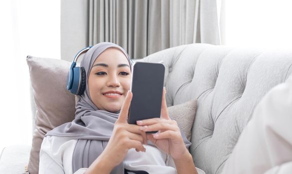 Close-up image, Attractive Muslim woman using a smartphone in living room, chatting with her friends or scrolling on online shopping website..