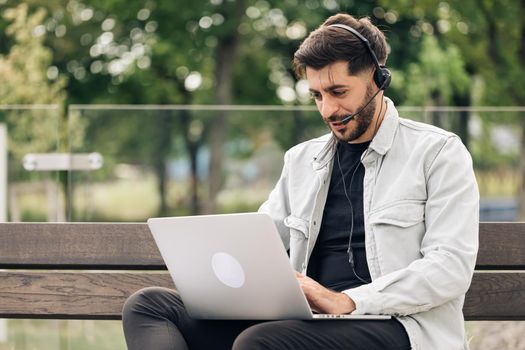 Young caucasian business man wearing headphones communicating by video call. Ethnic businessman speaking looking at laptop computer, online conference distance office chat, virtual training concept.