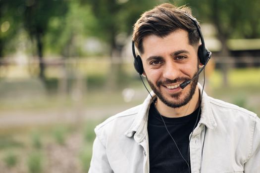 Close up of Face young handsome man operator look at camera smile taking calls smile outdoor call center office business worker computer corporate headset job service group finance phone