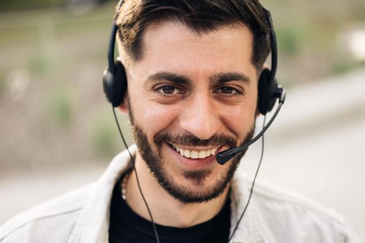 Close up of Face handsome man operator look at camera smile taking calls smile outdoor call center office business worker computer corporate headset job service group finance phone.