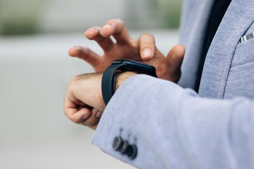 Closeup shot of male's hand uses of wearable smart watch at outdoor. Smartwatch on a business man's hand outdoor. Gorgeous businessman touching a smart watch. Smart watch.