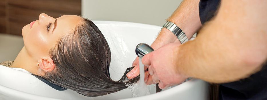 Male hairdresser rinses hair of young woman after shampooing at hair salon