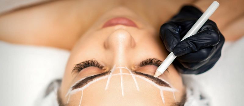 The beautician marks the eyebrow with a white pencil to prepare a permanent makeup procedure