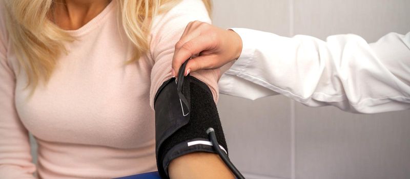 Nurse or female doctor puts on tonometer on arm of young woman in the hospital