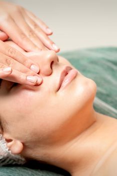 Young woman getting facial massage with closed eyes by beautician in beauty salon
