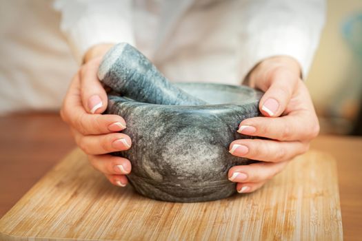 Mortar and pestle in the female hands on the cutting board