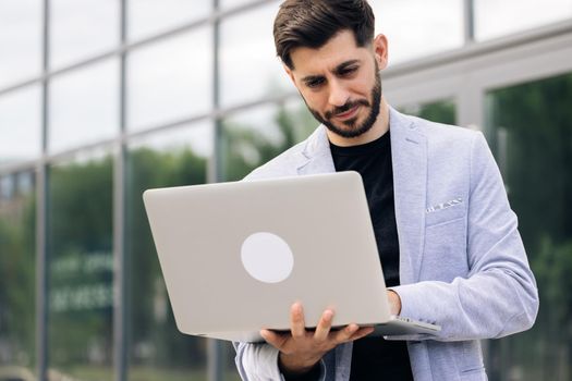 Caucasian handsome man trader working at laptop checking stock market data, looking at computer. Male successful broker with smile. Businessman.