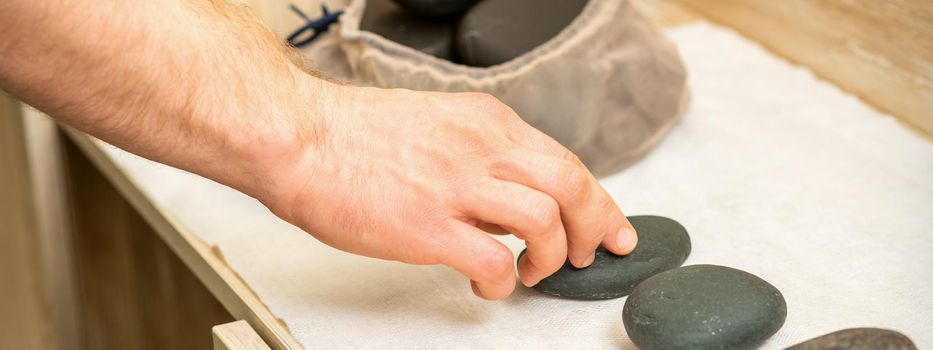 Hand of masseur takes hot black massage stones from the table in spa