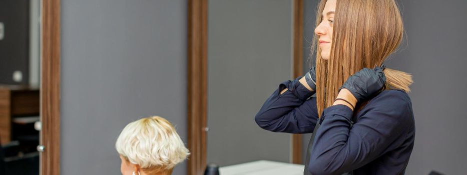 Female hairdresser puts on black apron before cutting the client's hair