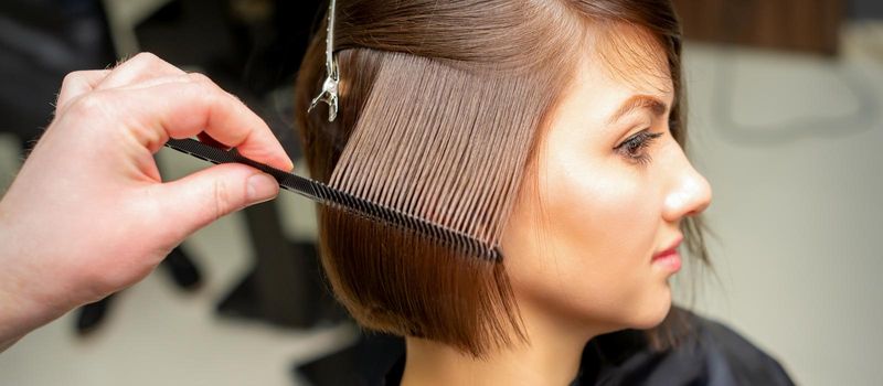 Professional hairdresser brushing straight female hair while hair care beauty procedures in a hair salon