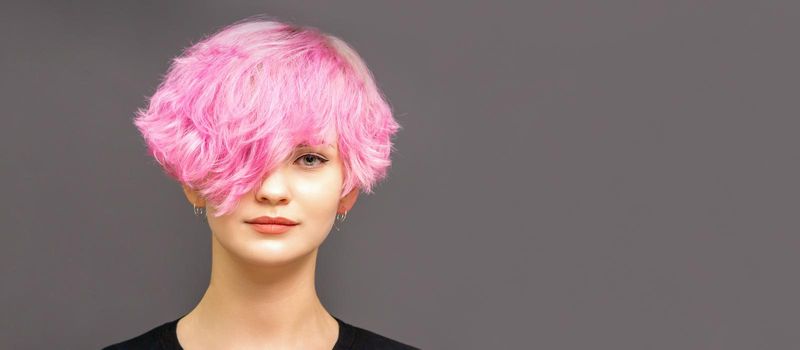 Portrait of fashion model young woman with stylish dyed pink hair in black clothes on dark background