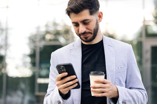 Smiling young attractive bearded man walking use smartphone look around at city center. Handsome man messagen stylish. Employment technology.