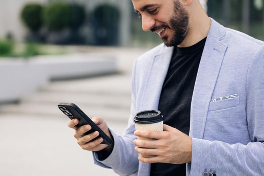 Young elegant bearded man using social media application on smartphone text messages receive news smiling outdoor. People portraits. Technology.