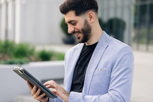 Happy face looking tablet screen outdoors. Elegant male chatting online with digital device outside. Businessman holding tablet in hands using business apps on tablet computer.