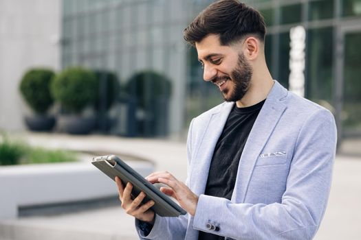 Beautiful young man engaged in business using tablet computer reading financial news online. European hairstyle. Corporate people.