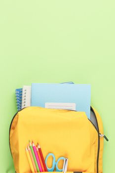Back to school concept. School backpack with educational supplies on a green background. Top view. Flat lay student desk.