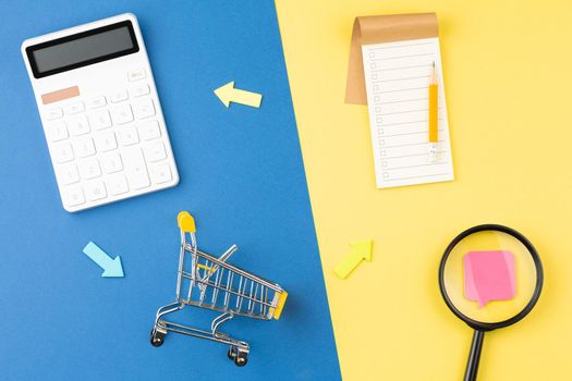 Supermarket trolley with calculator and shopping list. Discounts and promotions concept. Flat lay.