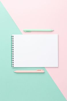 White sheet spiral notebook with a blue and pink pen on a two color background. Top view. Spring concept.