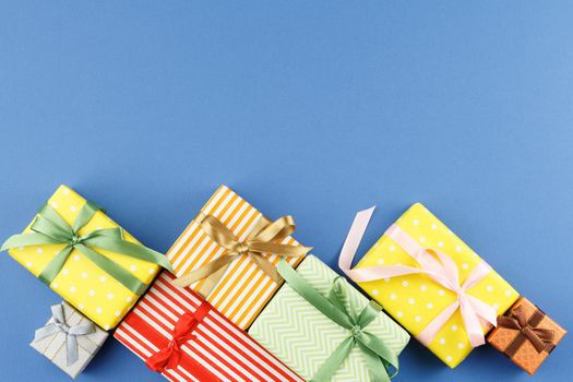 Gifts in colorful wrapping paper with ribbon bows on blue isolated background. Flat lay. Festive present concept. Top view.