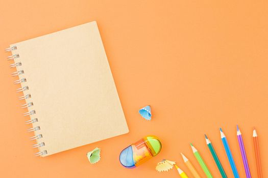 Spiral craft notebook with colored pencils sharpener and shavings on an orange background. Top view, copy space.