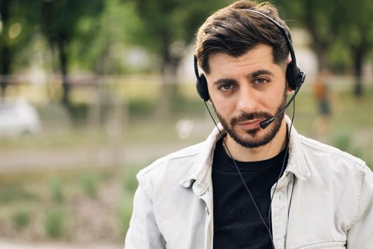 Young handsome bearded man employee in headset with microphone, working in the customer service department, looking at the camera, talking to customers on a helpline