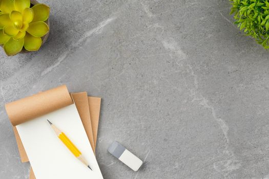 Open notepad with pencil, glasses, elastic band and flower in pot on gray marble background. Top view.