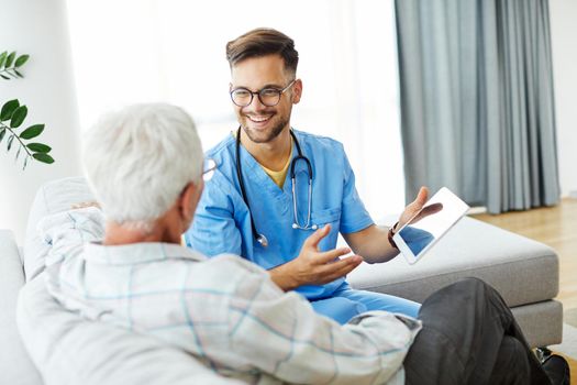 Doctor or nurse caregiver helping senior man with a tablet at home or nursing home