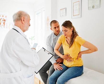 Senior doctor talking to young couple in his office in clinic