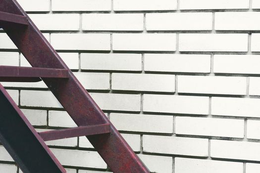 a structure consisting of a series of bars between two upright lengths of wood, metal used for climbing up or down.Part of the stairs red metal ladder leading up against of a white brick wall