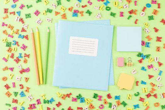 School notebook with colored pencils on a background of multicolored wooden letters. Flat lay. Back to school concept. Paper stickers on a green table. Top view.