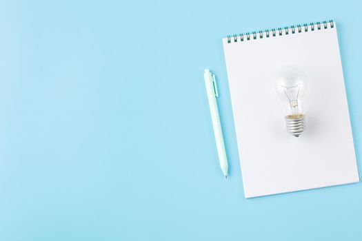Light bulb with a spiral notepad and pen on a blue background. Initiative of ideas concept of a business or some activity.