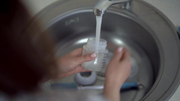 A young mother washes a bottle of baby food with a special brush. Close-up hands. 4k