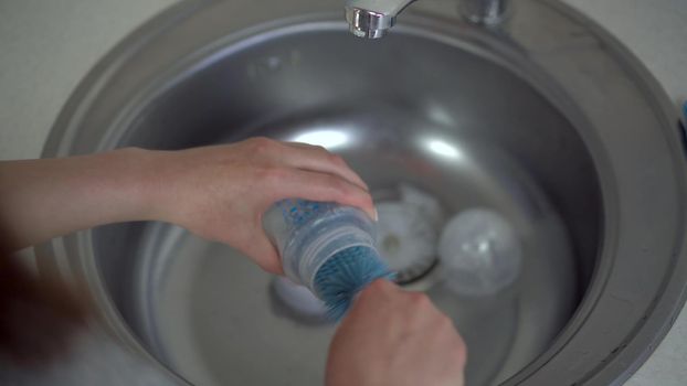 A young mother washes a bottle of baby food with a special brush. Close-up hands. 4k