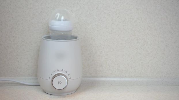 A woman puts a bottle of food into a bottle warmer. Apparatus for rapid heating and stirring of infant formula. 4k