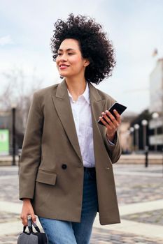 portrait of a smiling business woman walking with a smart phone in her hand, technology and communication concept