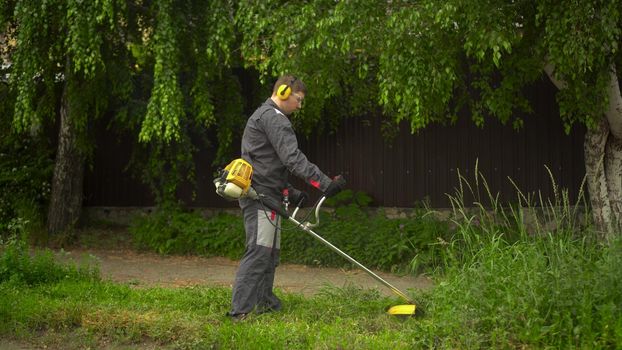 A young man from the special services mows the lawn with a petrol trimmer. A man in glasses and headphones with a lawn mower in his hands. 4k