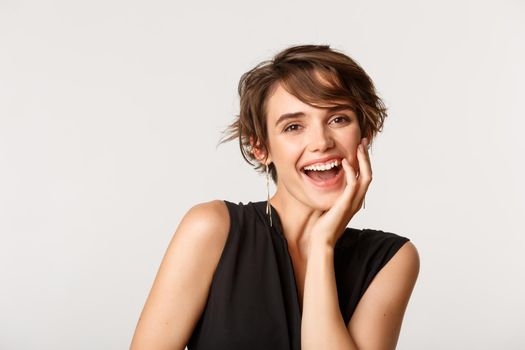Gorgeous elegant woman laughing flirty and touching face, standing over white background.