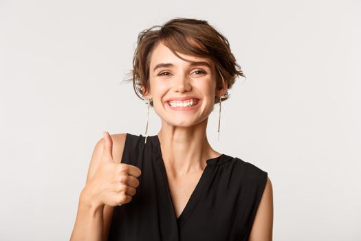 Close-up of satisfied attractive woman showing thumbs-up in approval, like something, praising good job, standing white background.