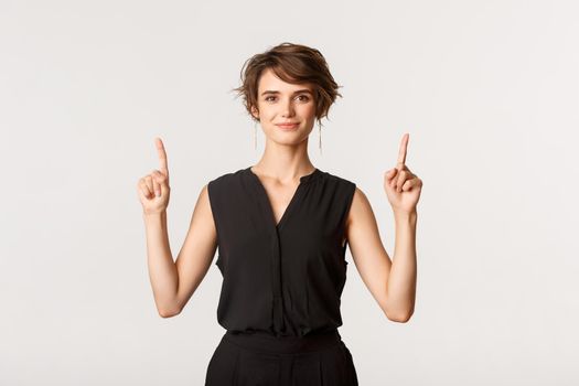 Image of confident attractive and stylish young woman pointing fingers up, showing logo, white background.