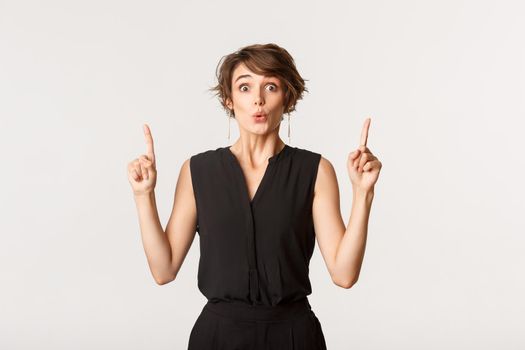 Image of surprised attractive woman looking impressed, pointing fingers up.