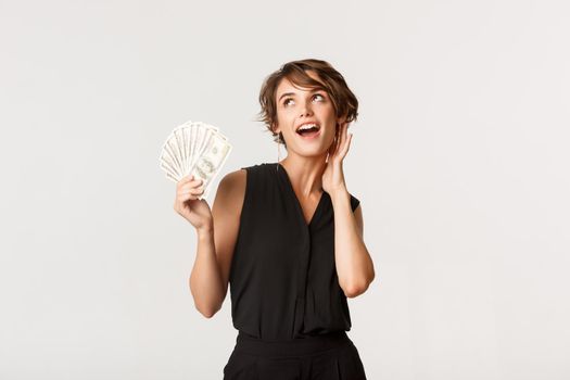 Gorgeous rich girl showing money and looking sassy, standing over white background.