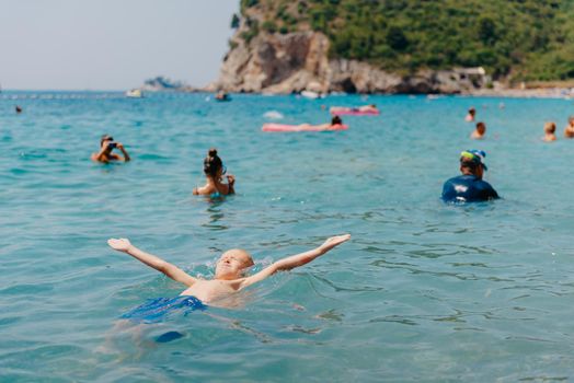 Child learning to swim in the open sea of tropical resort. Kids learn swimming. Exercise and training for young children. Little boy with colorful float board in sport club. Swimming baby or toddler. Happy child boy swims in sea in swimming circle with splash. Blue sky and water. Swimming training. Fun joy activities on vacation in the beach. Childhood moments lifestyle. Freedom careless. boy swim in the sea.