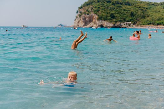 Child learning to swim in the open sea of tropical resort. Kids learn swimming. Exercise and training for young children. Little boy with colorful float board in sport club. Swimming baby or toddler. Happy child boy swims in sea in swimming circle with splash. Blue sky and water. Swimming training. Fun joy activities on vacation in the beach. Childhood moments lifestyle. Freedom careless. boy swim in the sea.