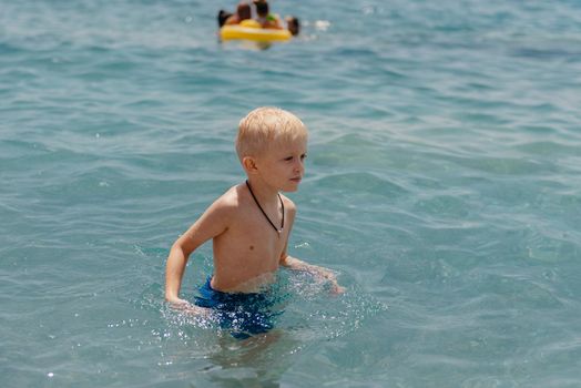 Child learning to swim in the open sea of tropical resort. Kids learn swimming. Exercise and training for young children. Little boy with colorful float board in sport club. Swimming baby or toddler. Happy child boy swims in sea in swimming circle with splash. Blue sky and water. Swimming training. Fun joy activities on vacation in the beach. Childhood moments lifestyle. Freedom careless. boy swim in the sea.