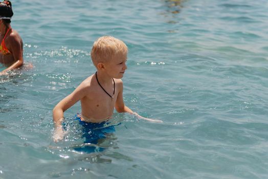 Child learning to swim in the open sea of tropical resort. Kids learn swimming. Exercise and training for young children. Little boy with colorful float board in sport club. Swimming baby or toddler. Happy child boy swims in sea in swimming circle with splash. Blue sky and water. Swimming training. Fun joy activities on vacation in the beach. Childhood moments lifestyle. Freedom careless. boy swim in the sea.